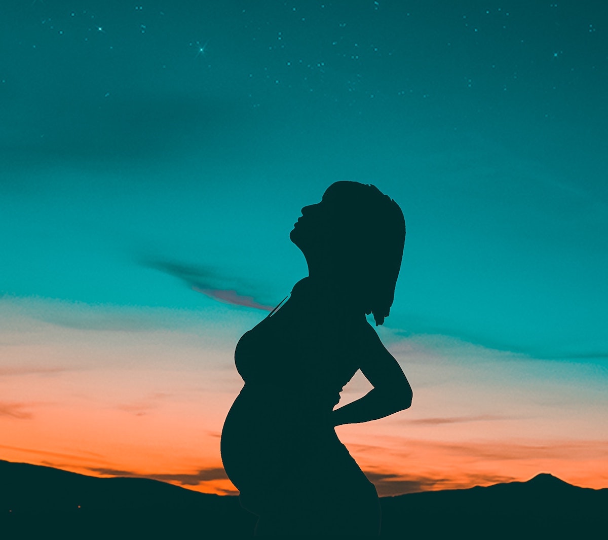 Pregnant woman standing outside against a sunset.